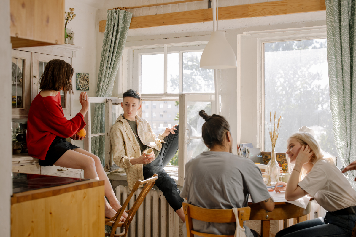 The image shows four people in a living room, symbolizing life with roommates.